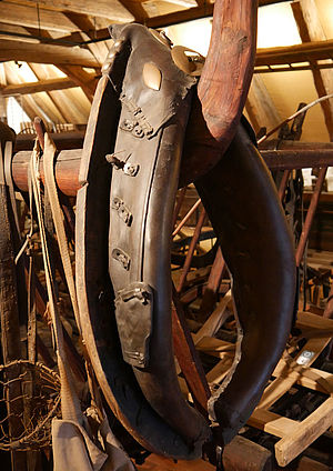 An einer Stange hängt ein Kummet. Das ist ein großer ovaler Ring aus Holz, Leder und Metall. Er wurde eingesetzt, damit Zugtiere schwere Lasten ziehen konnten.  