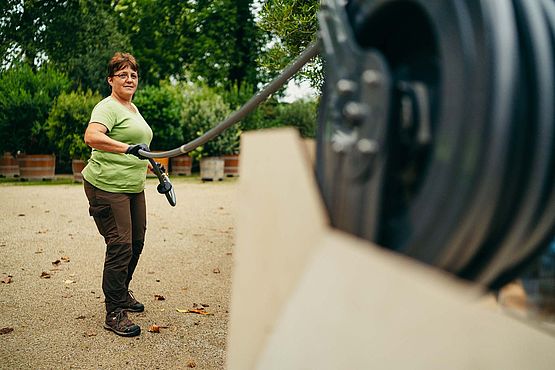 Eine Gärtnerin bei der Arbeit mit dem Gießroboter, wie sie den Schlauch von der Rolle wickelt
