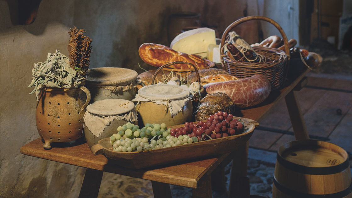 Ein Tisch vollgestellt mit Brot, Wurst, Krügen und Töpfen.